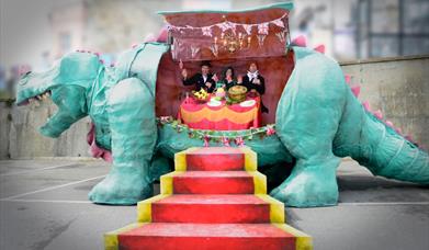 A model dinosaur cut open and inside its belly are three people sitting at a dining table eating