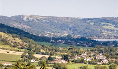 View across fields to a village, lake and rocky hills in the background