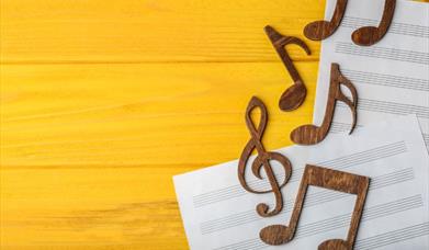 Two sheets of music on a wooden surface with some clefs and musical notes