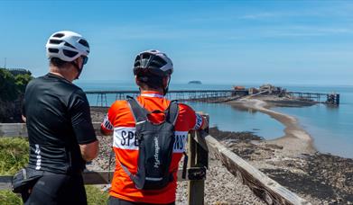 Two cyclists leaning against a fence admiring a sea view