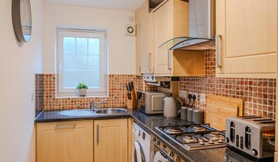 Kitchen inside the Seaside Apartments Weston-super-Mare featuring wooden units, appliances, tiles and a dark worktop