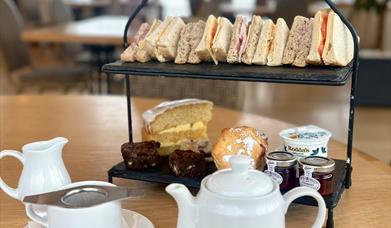 Traditional afternoon tea with pot of tea and cake stand with cakes and sandwiches