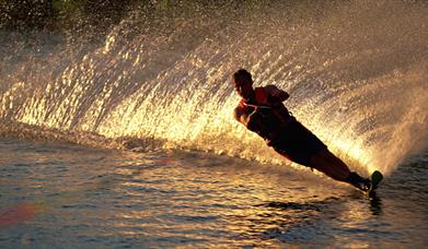 Silhouette of a water skiier with the golden glow of the wash behind him at sunset