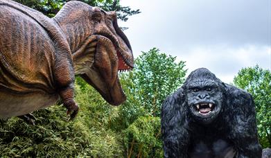 An animatronic dinosaur at Wookey Hole staring at a giant model gorilla