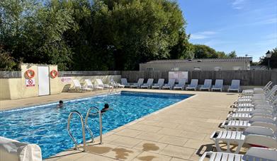 Outdoor swimming pool on a sunny day with two people swimming and lots of empty sun loungers