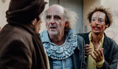 2 clowns looking at another, one is pleading