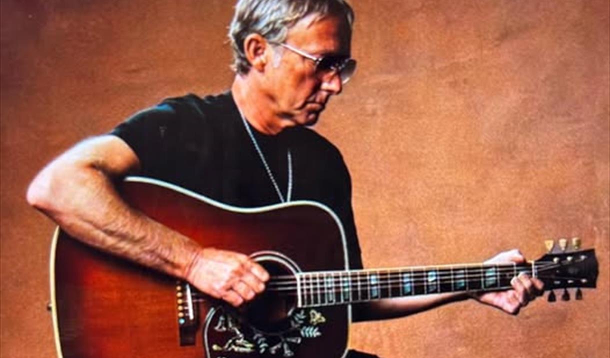 Guitarist Steve Craddock dressed all in black sitting down and playing his guitar