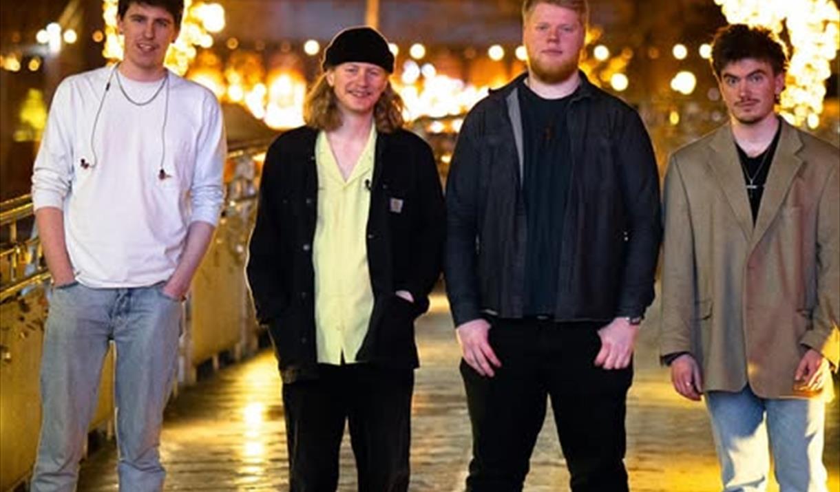 Four members of the Instigators Band standing in a shopping centre with Christmas lights behind them