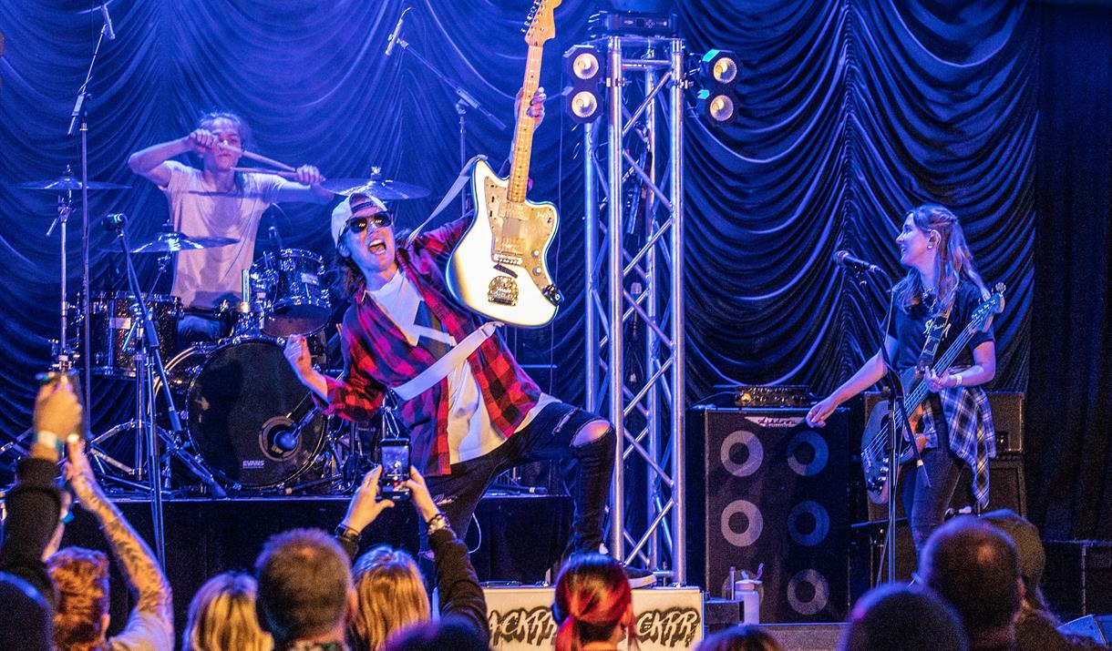 A guitarist in front of a large crowd hold his electric guitar aloft by its neck