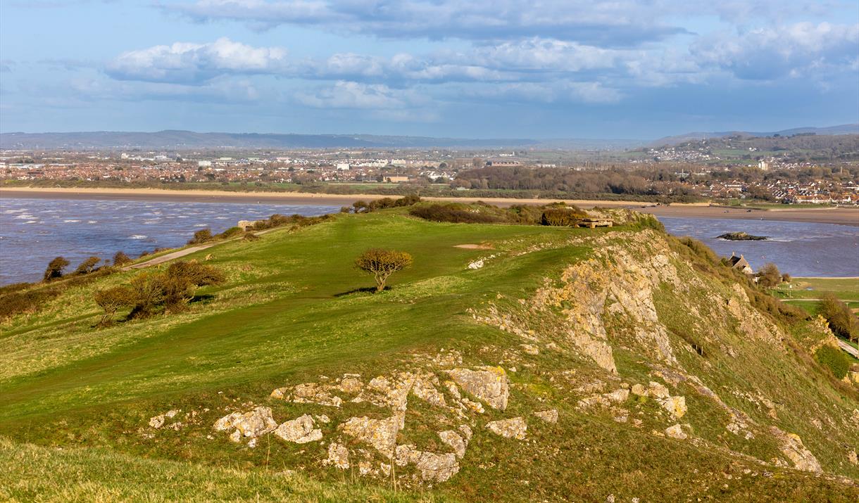 View over the top of a grass-topped rocky cliff with sea on either side and a shoreline in the background