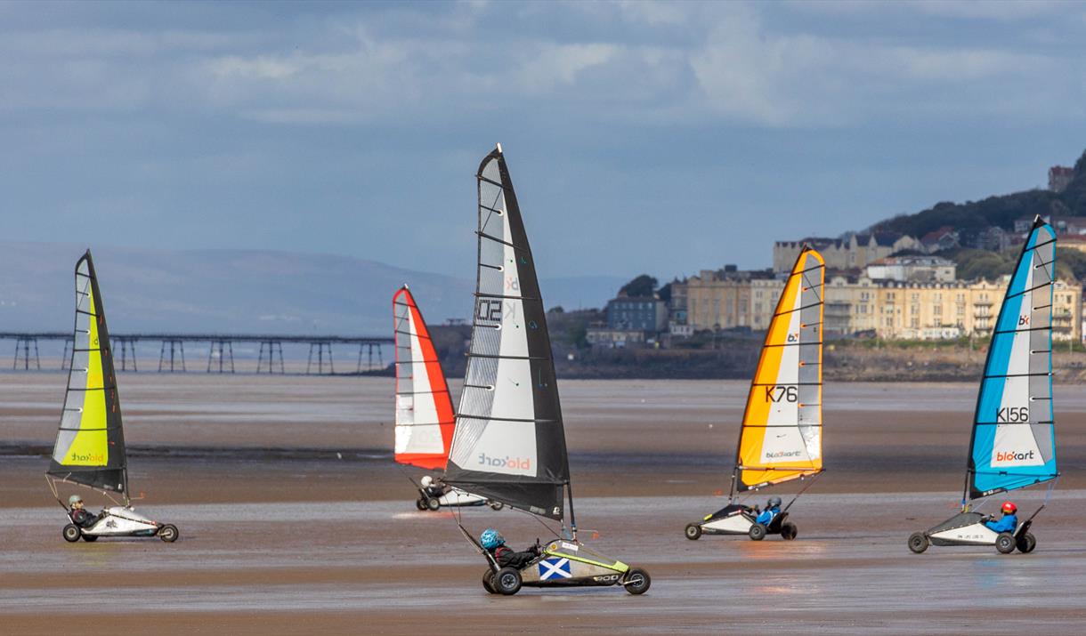 Five Blokarts with their colourful high sails racing across the sandy beach at Weston-super-Mare