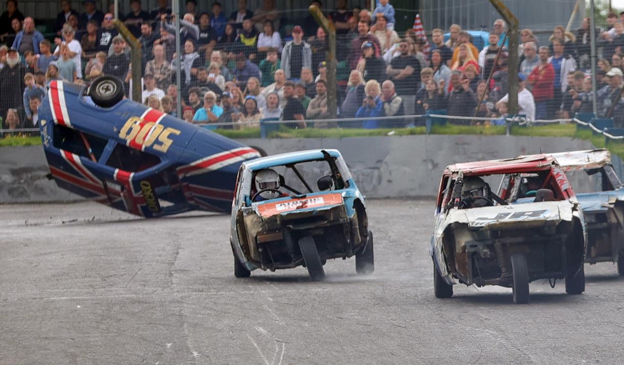 A banger racing car on its roof with three other three-wheeler cars in front