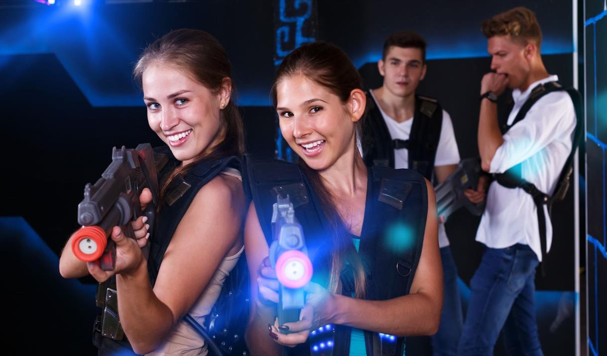 Two girls firing laser guns with two males in the background