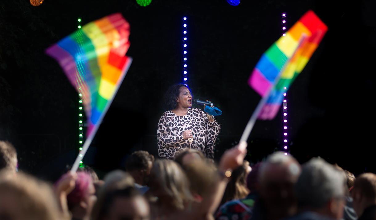 A singer on stage in front of a large crowd waving two Pride flags