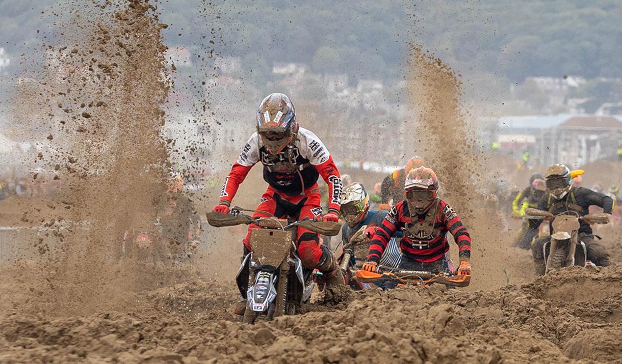 Sand flies up as three motorbike riders struggle through sand in a beach race