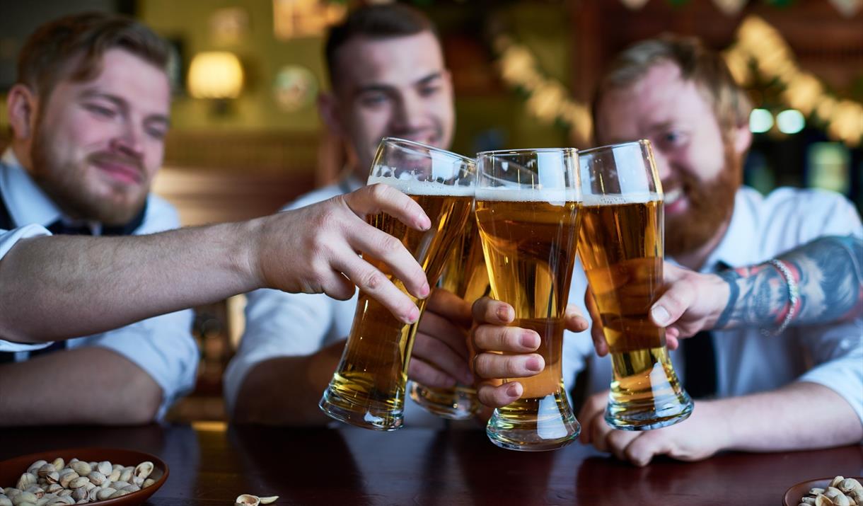 Three men in a pub clinking their full pint glasses