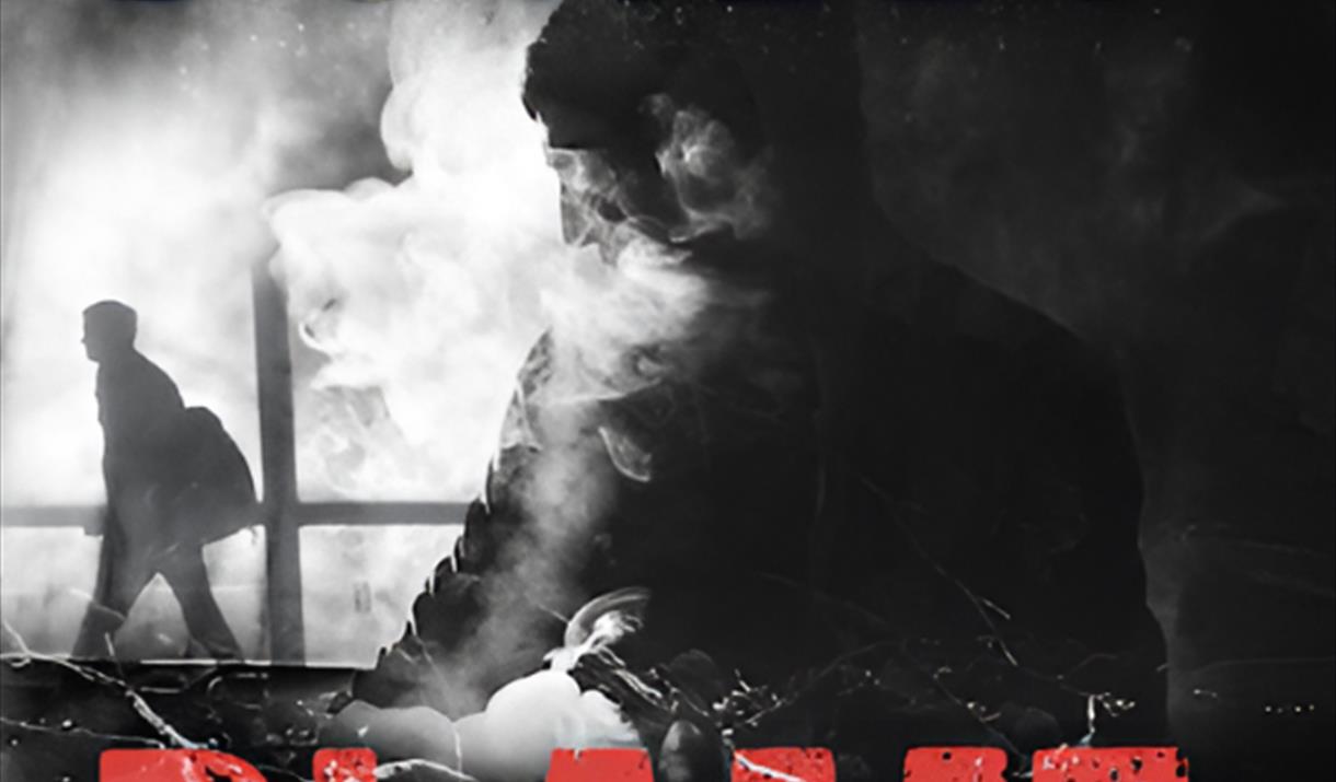 A man walking in smoke to the left. A man face towards the back in the shade. The background is black with the title is red and small information is g