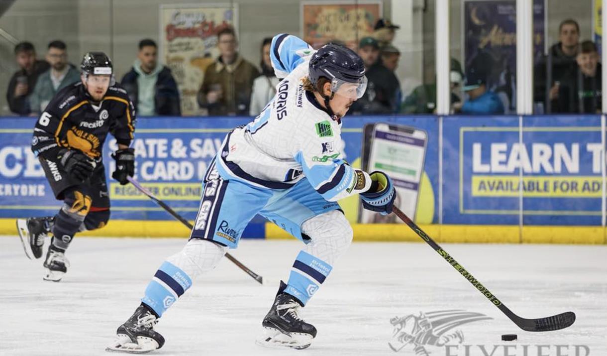 A Bristol Pitbulls ice hockey player in their light blue and white kit comes away with the puck