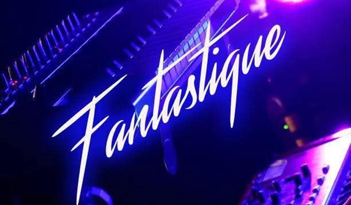 The word Fantastique written in white and slanting upwards across a blue background photo featuring some music decks