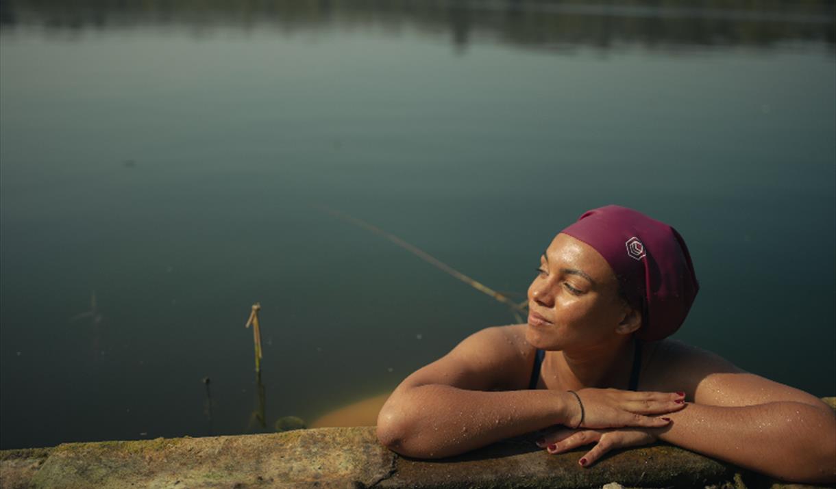 Woman in swimcap, arms drapped over pool edge, looking happy