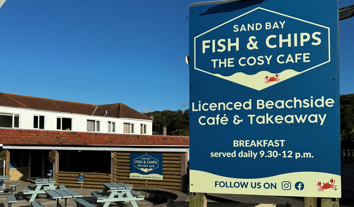 Close up image of the Sand Bay Fish & Chip shop sign against a blue sky with the premises in the background