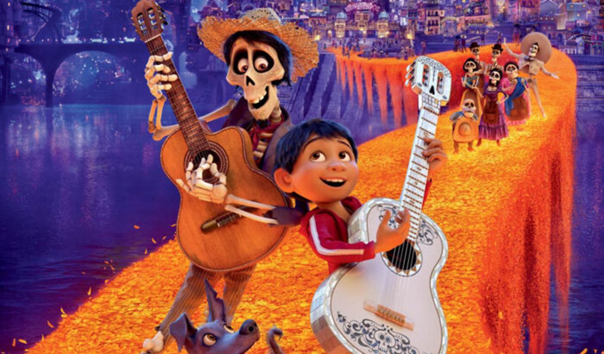 The poster for the film Coco which features and child and a skeleton playing a guitar. The characters in the background suggest the Mexican Day of the