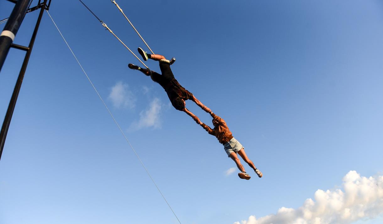 2 people on a trapeze, flying through the blue sky