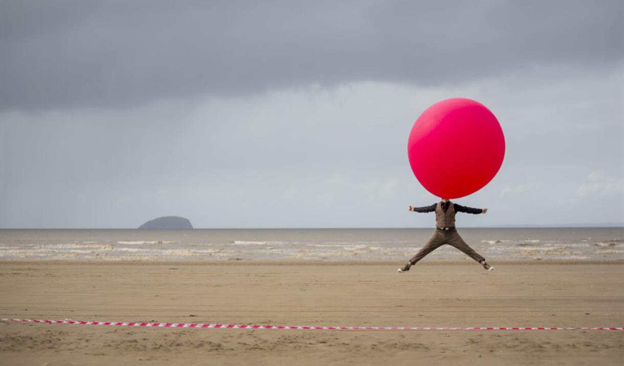 A man on the beach with a giant balloon over his head.