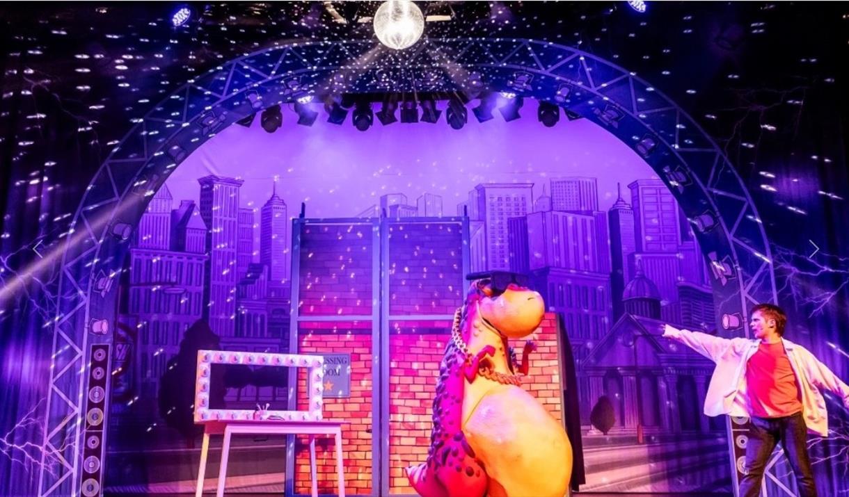 A man on stage pointing at a giant toy dinosaur