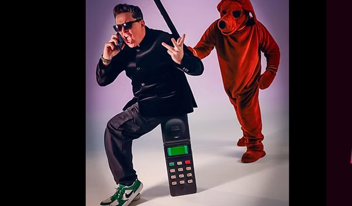TV star Dom Jolly sitting on a giant mobile phone with a person in a dog costume about to push him over