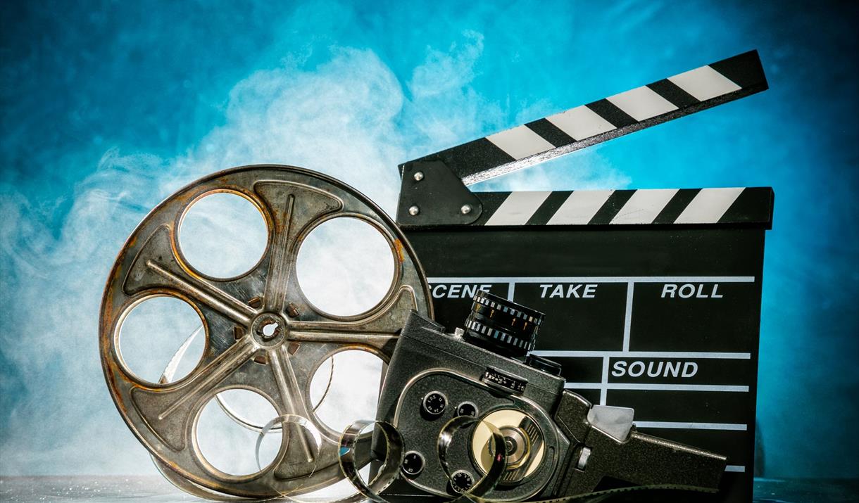 Clapper board, old film reel and vintage camera set against a blue background