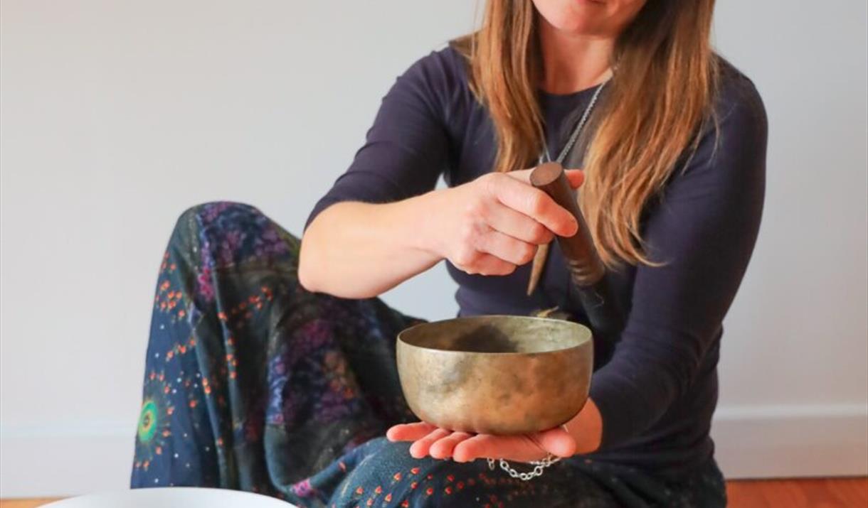 A person sat on the floor using a singing bowl. There are other bowls around them