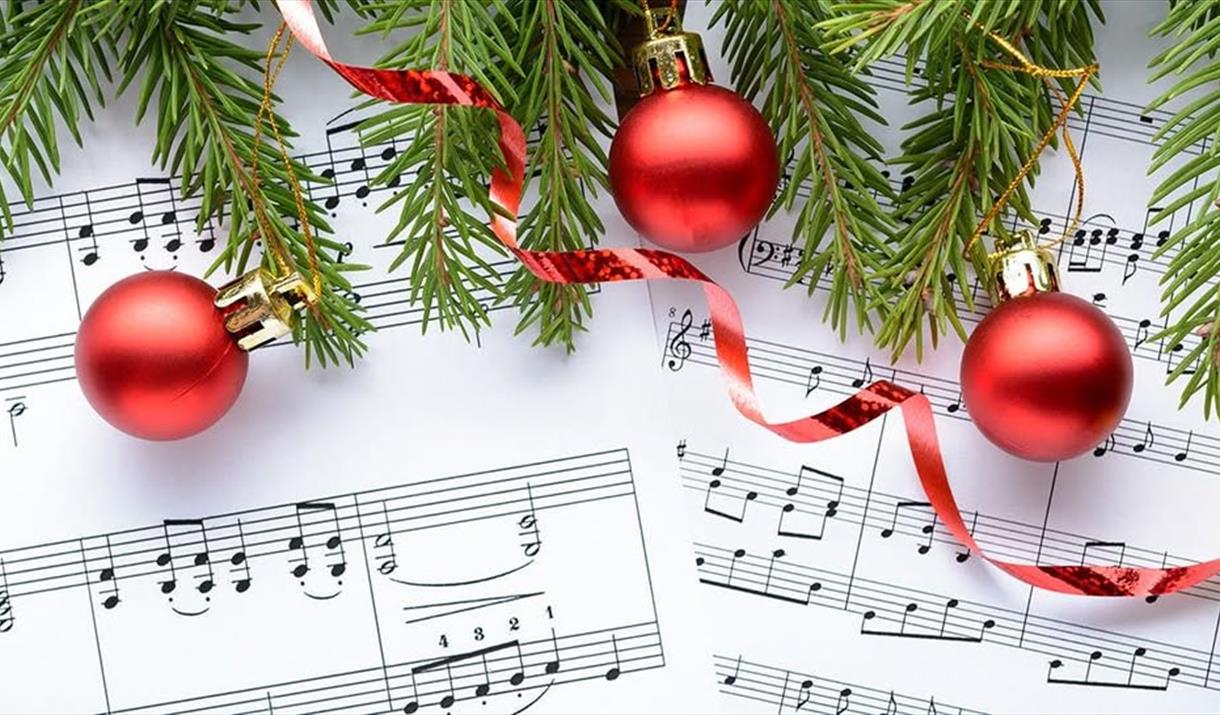 Red Christmas baubles and the branches of a Christmas tree overlaid on a sheet of music