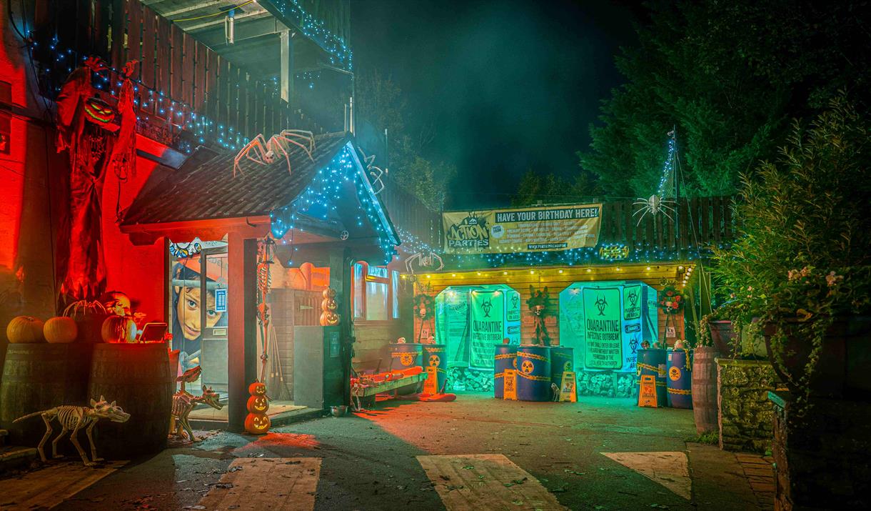 Mendip Activity Centre's outdoor reception area at night - decorated with Halloween decor, pumpkins, giant spiders, zombie apocalyptic banners and red