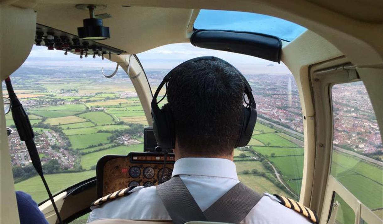 View from the back seat of a an airborne helicopter showing the pilot, cockpit and view