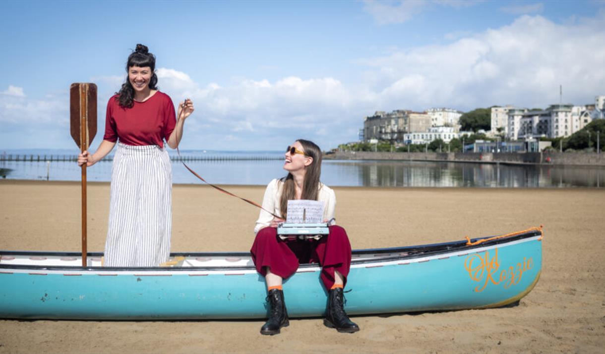 Photograph of Beth Calvery and Beth Roberts sat in a blue boat on the beach at Marine Lake.