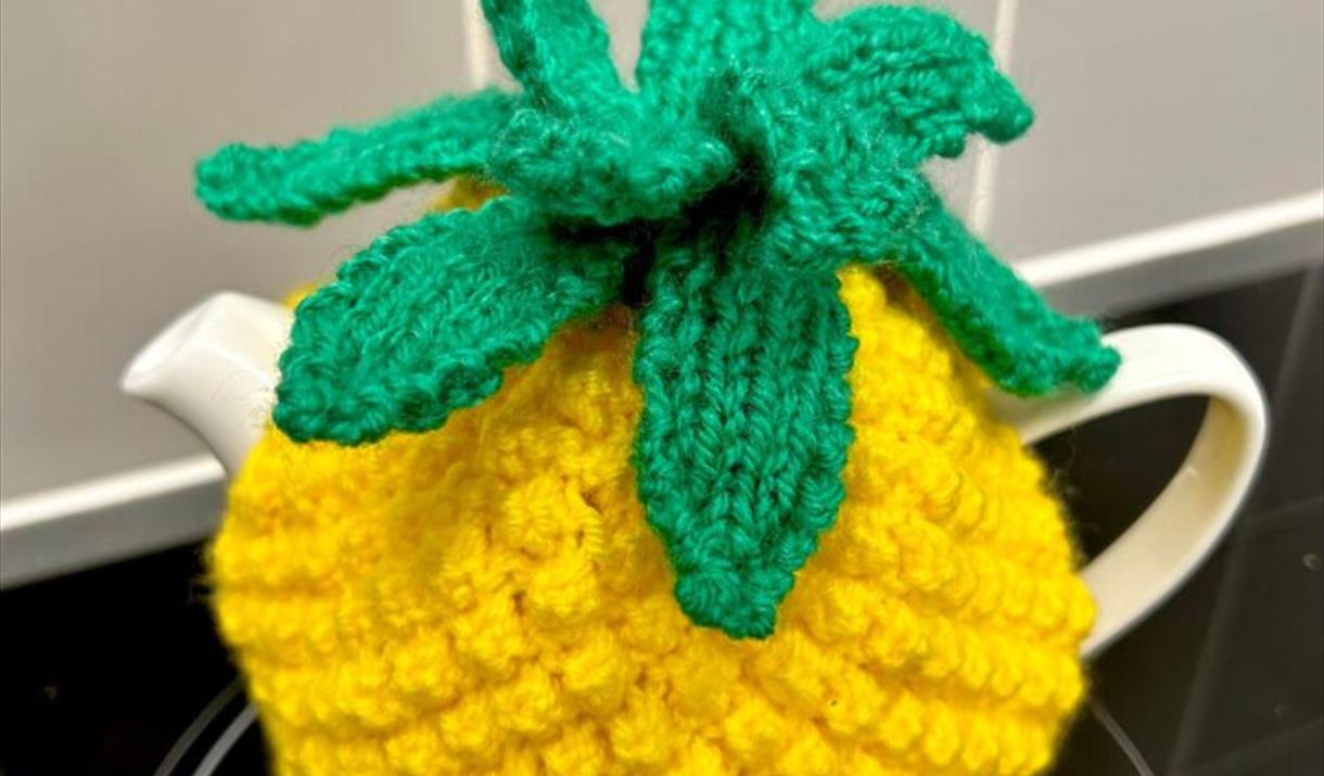 Photograph of a yellow hand-knitted tea cosy