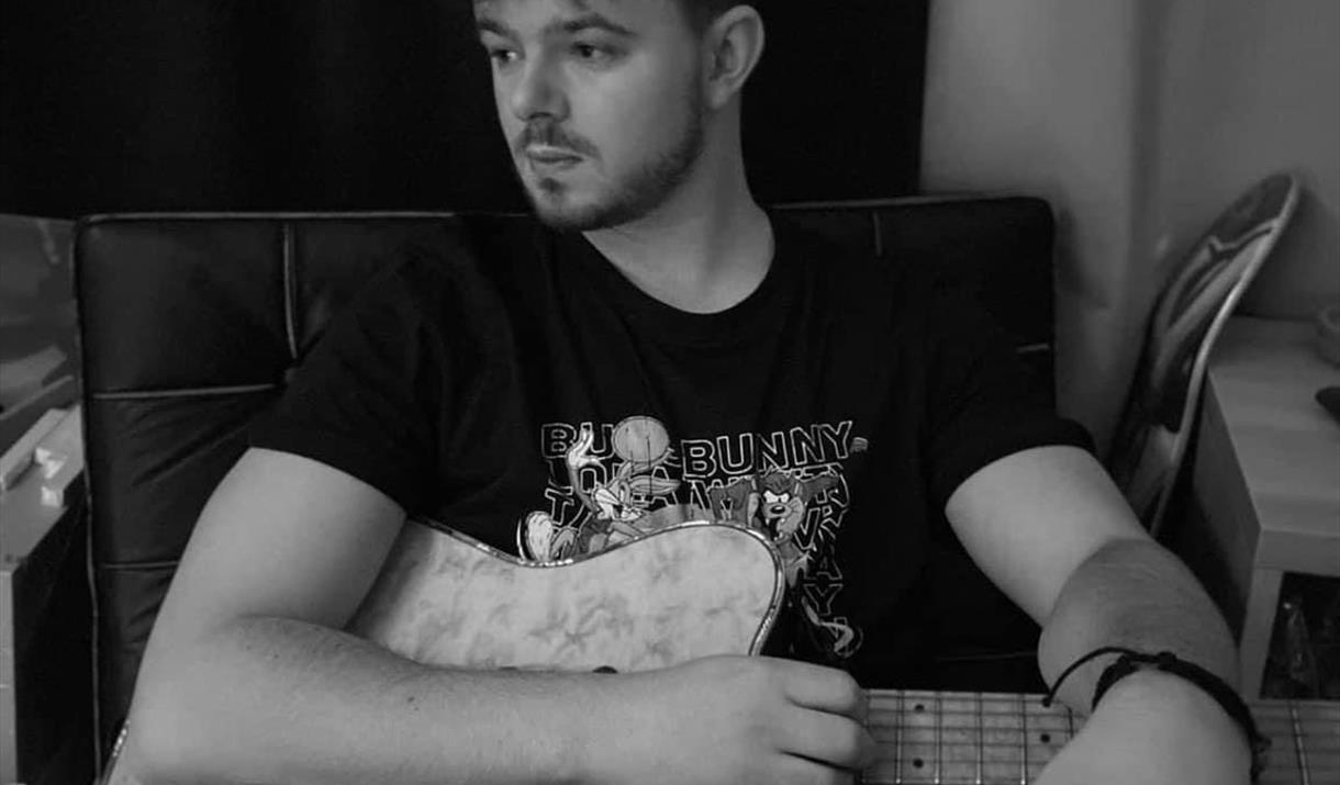 Black and white image of Luke Potter sat with an electric guitar and event information.