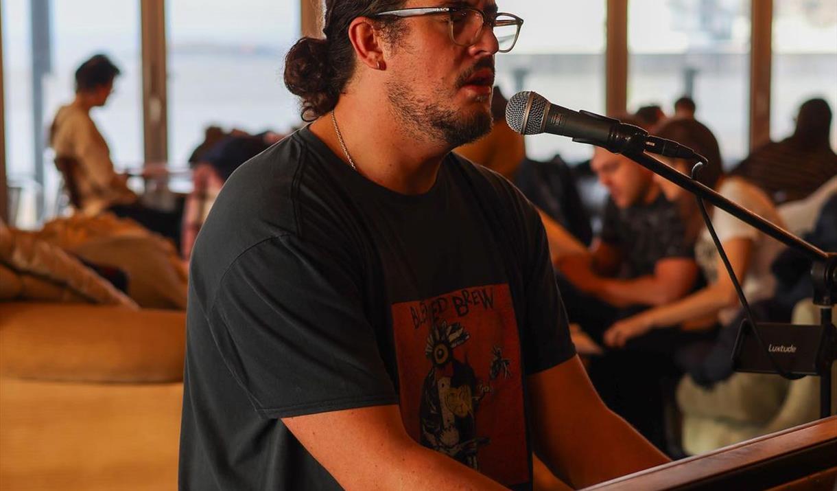 Photograph of Harrison singing into a microphone and playing a piano