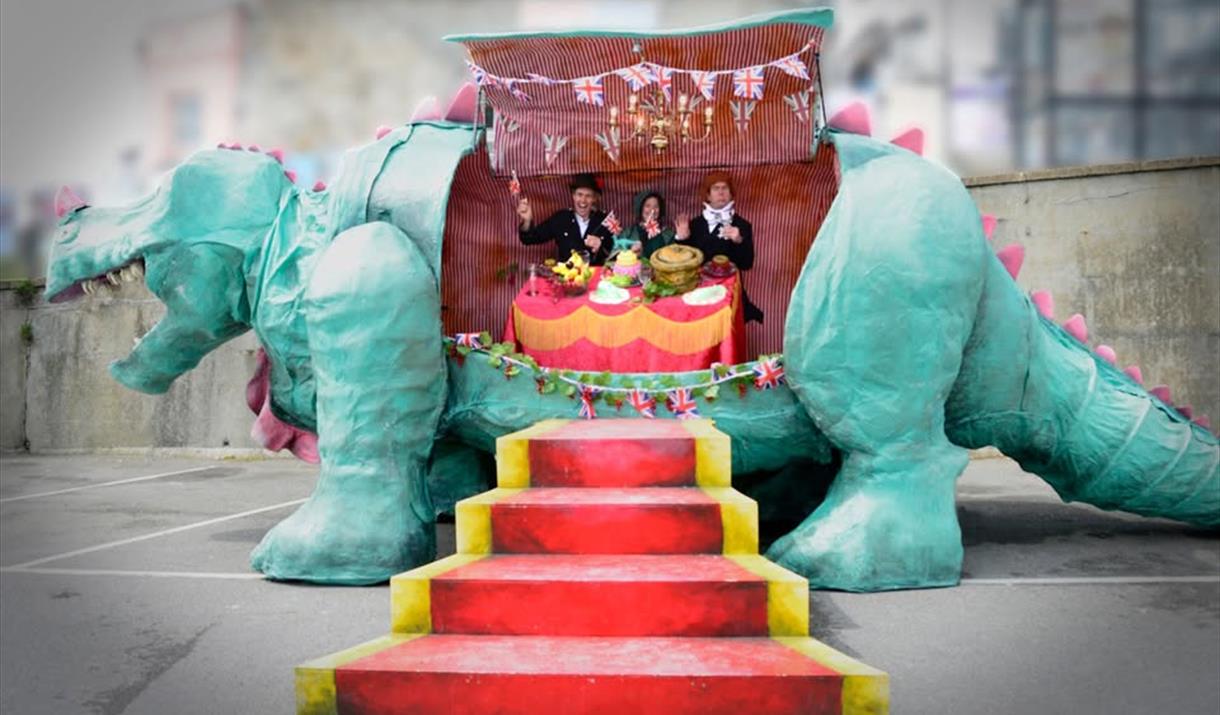 A model dinosaur cut open and inside its belly are three people sitting at a dining table eating