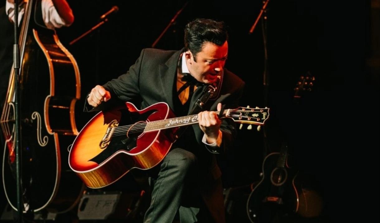 A guitarist wearing a black suit performing on stage