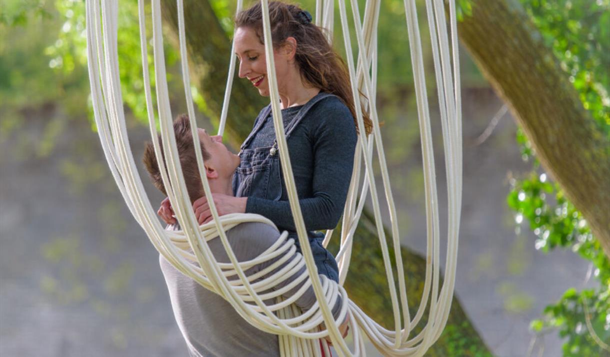 A man and woman in a romantic pose in a rope chair hanging from a tree