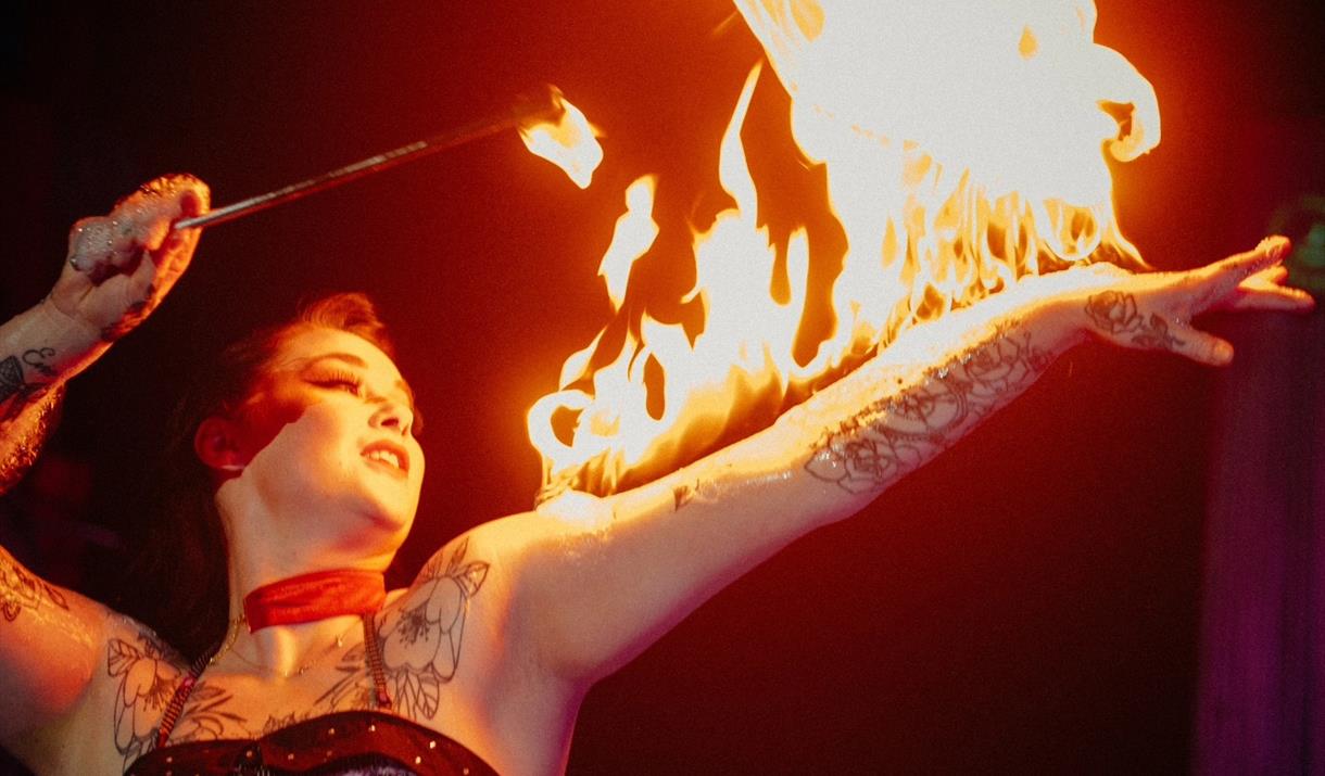 A circus performer with a fire stick and fire on her arm