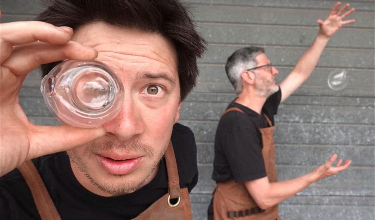 One man looking through glass and another juggling a glass