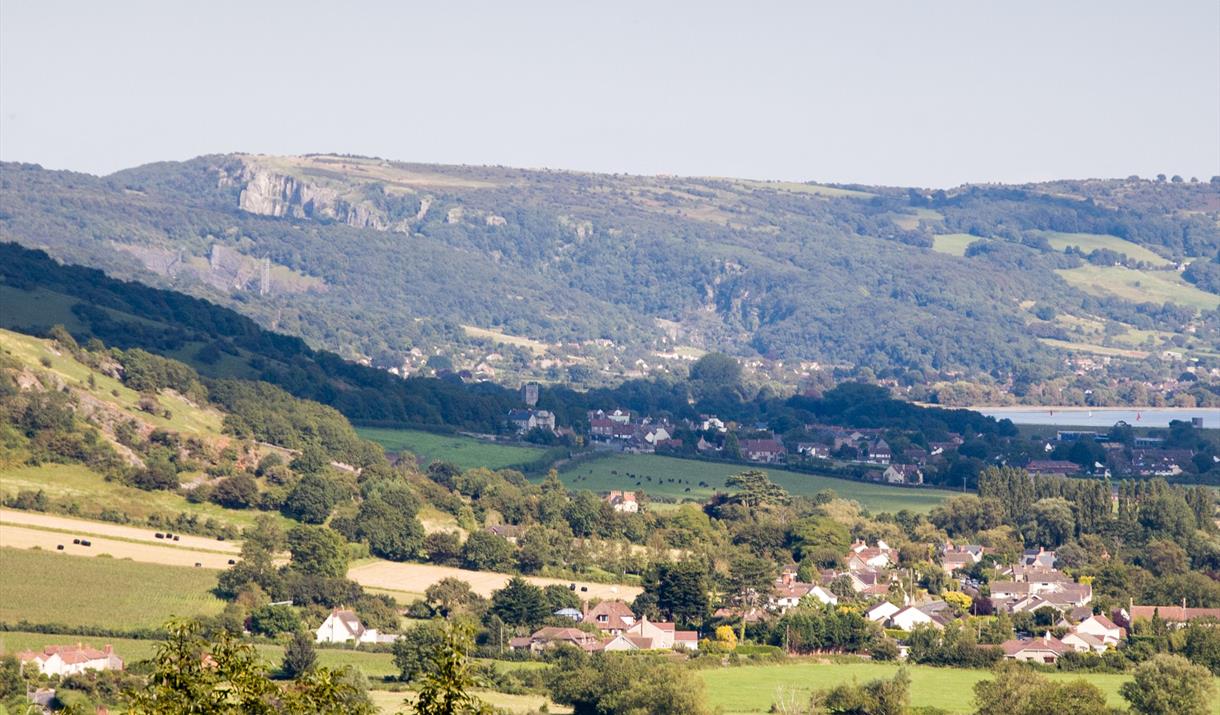 View across fields to a village, lake and rocky hills in the background