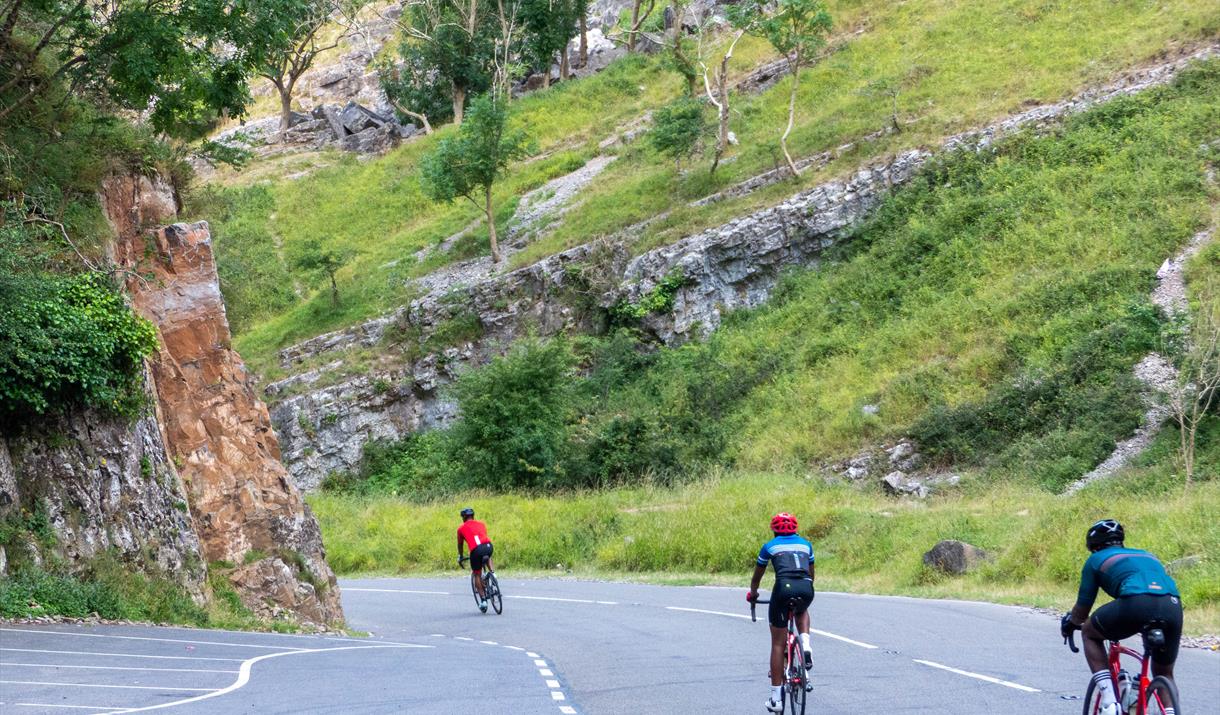 Three cyclists ride down a road in the centre of a gorge