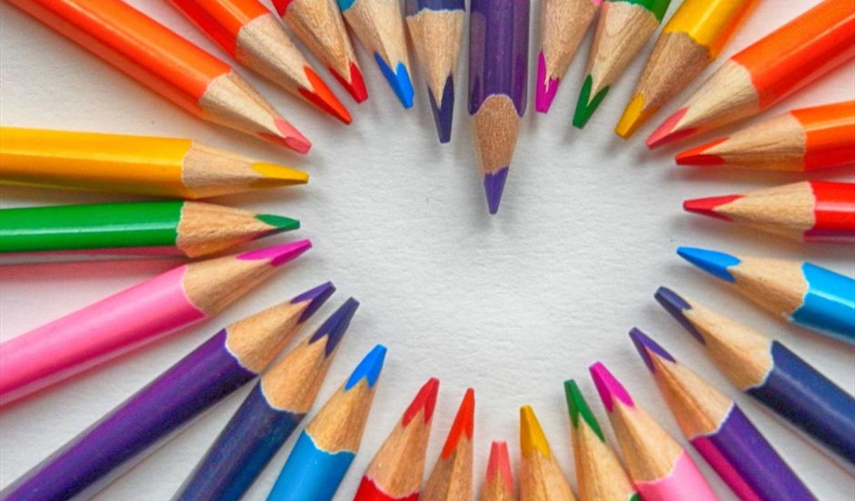 An arrangement of brightly coloured pencils creating a white heart shape in the middle