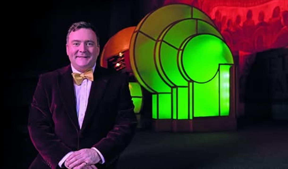 Organist Donald MacKenzie in a suit and bow tie, standing next to a Compton Organ