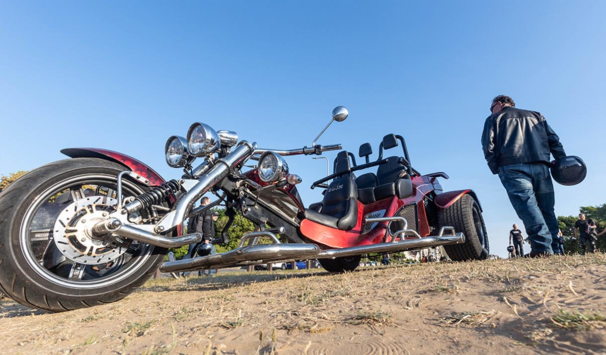 A leather clad biker walks past a motor trike