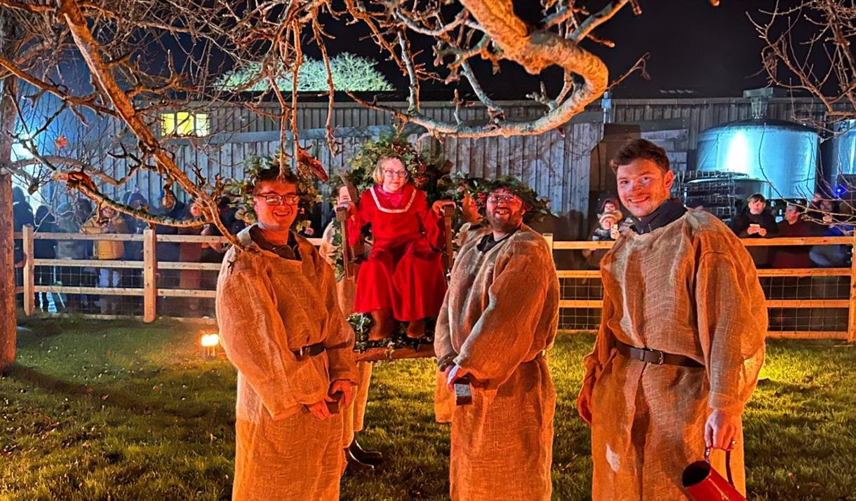 A night time Wassail ceremony featuring four men in traditional dress and someone sitting on a swing